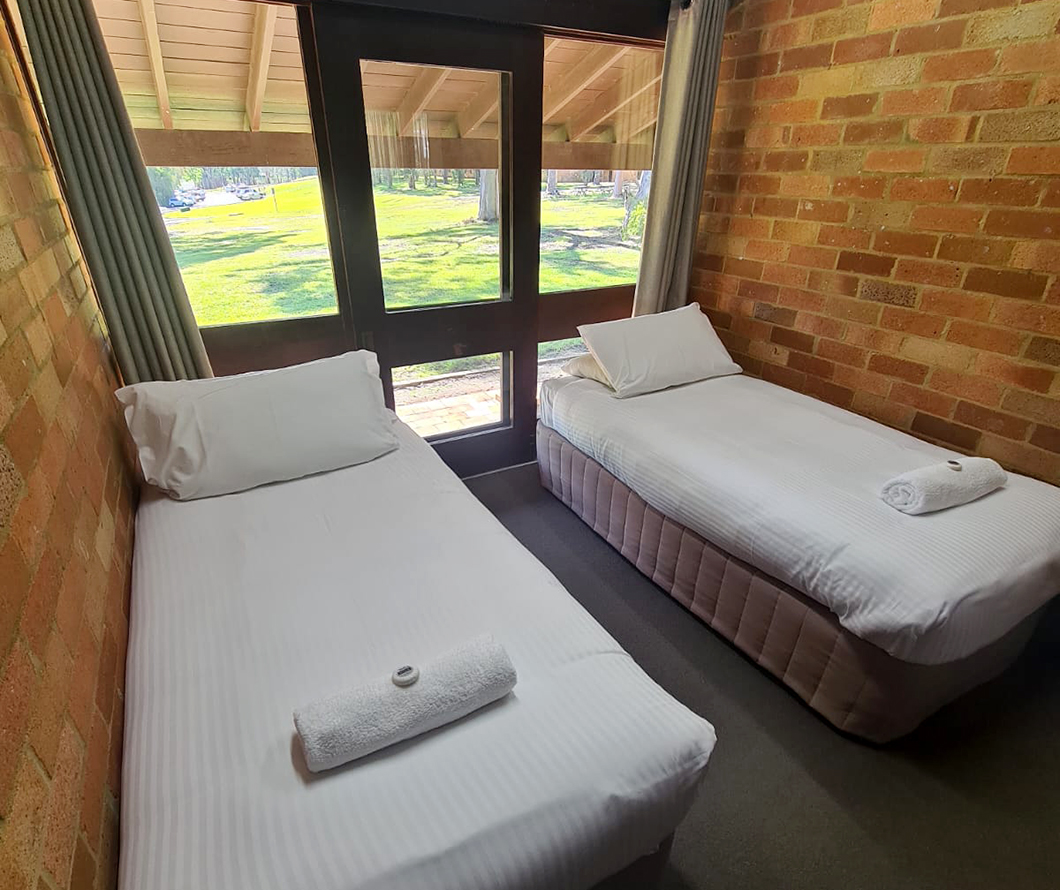 2 single beds with white linen in a room with large windows and a glass door