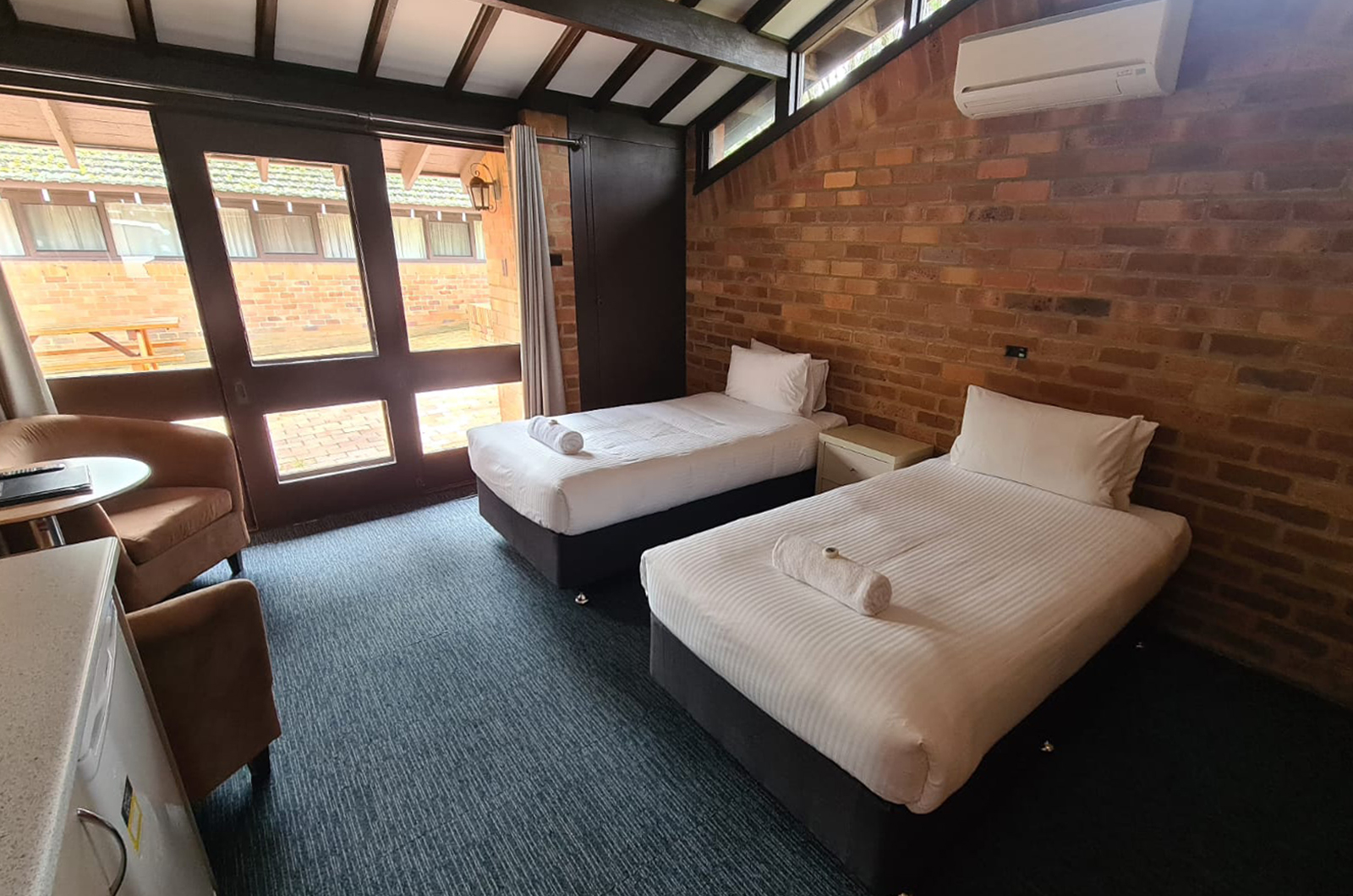 2 single beds with white linen and other furniture in a room with large windows and a glass door